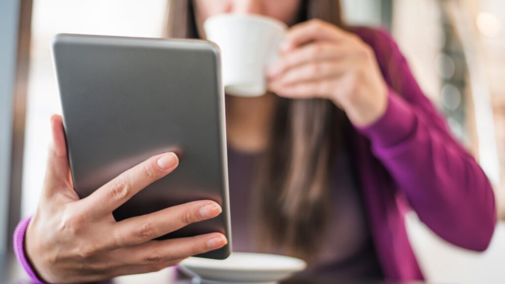 Mulher usando um tablet enquanto toma café, simbolizando a multitarefa e o consumo de conteúdo digital em dispositivos móveis.