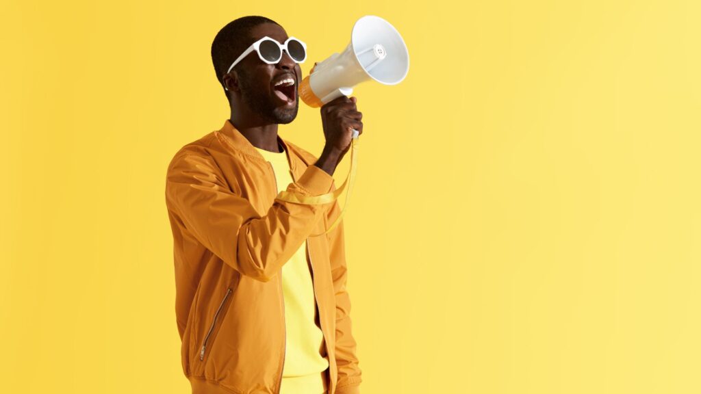 Homem energético falando através de um megafone contra um fundo amarelo vibrante, representando comunicação ativa e marketing de influência.